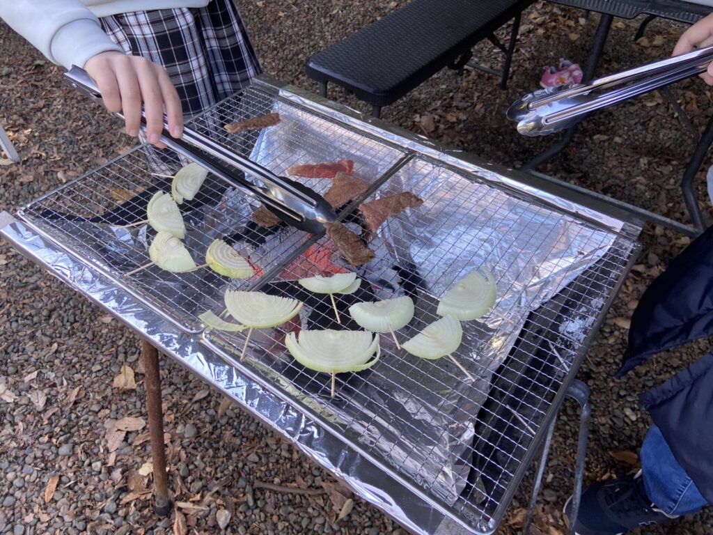 網に野菜と肉を置いて炭火で焼く様子